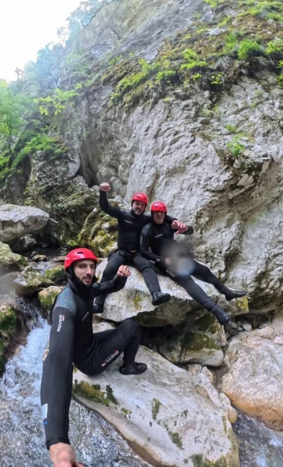 Canyoners in red helmets on mossy boulders beside the Komarnica river