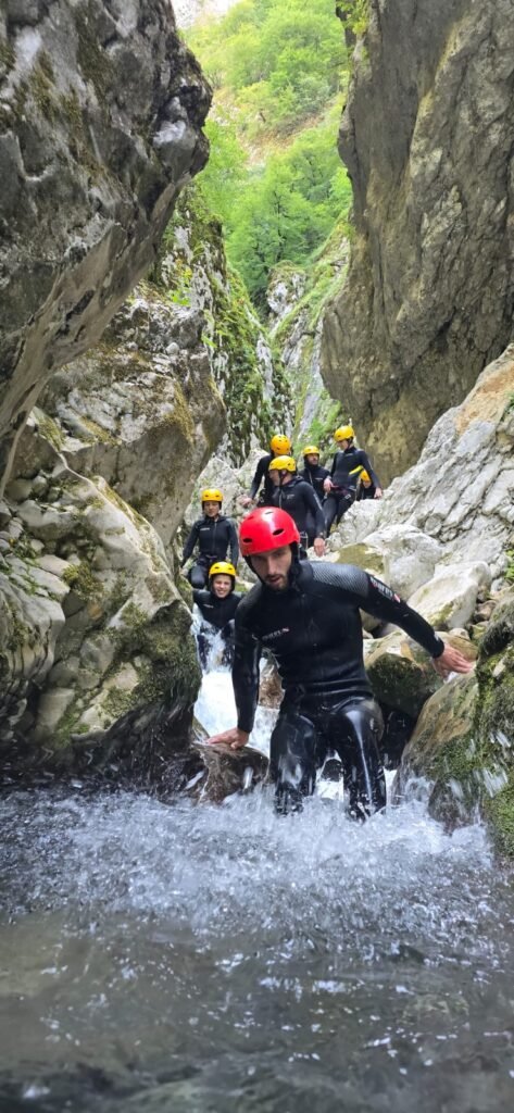 Canyoning group in wetsuits and helmets climbing through a waterfall in Nevidio Canyon