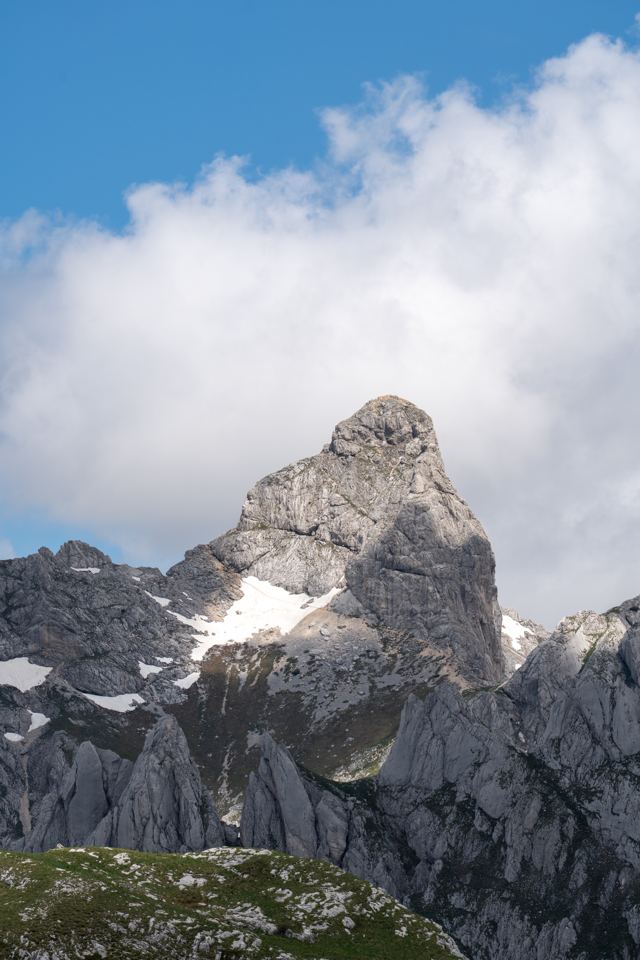 Rocky Durmitor peak with patches of snow under summer clouds