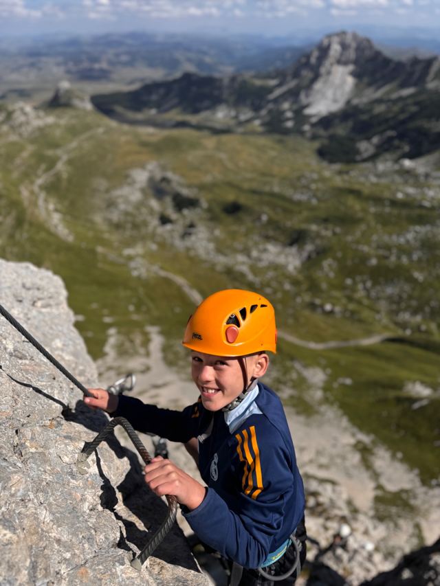 Smiling boy in an orange helmet climbing the via ferrata on Durmitor