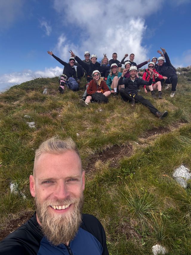 Selfie with a happy group in helmets on the grassy summit after the via ferrata
