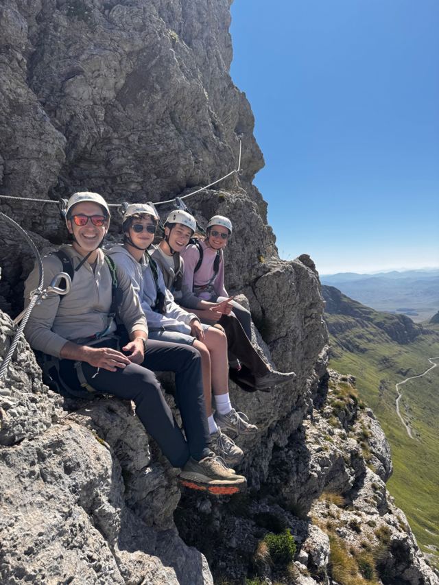 Family in helmets resting on a rock ledge along the via ferrata cable