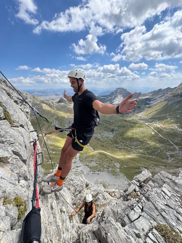 Climber on iron rungs with arms spread, high above the Durmitor valley